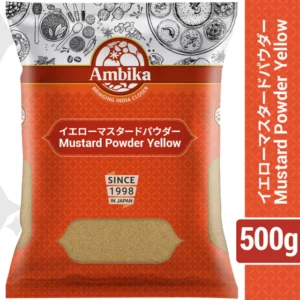 A 500g plastic pouch of Ambika Yellow Mustard Powder featuring an orange patterned background, white and English/Japanese text, and a clear product window showing the ground spice.