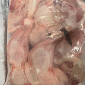 A thick clear plastic commercial freezer bag containing flat packed raw frozen chicken leg quarters stored inside a supermarket freezer rack.